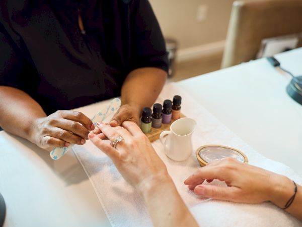 A manicurist tends to a client’s nails with several polish bottles and tools on a tidy table, focusing on nail care.