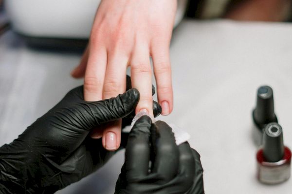A person's nails are being cleaned or polished by someone wearing black gloves, with nail polish bottles nearby.
