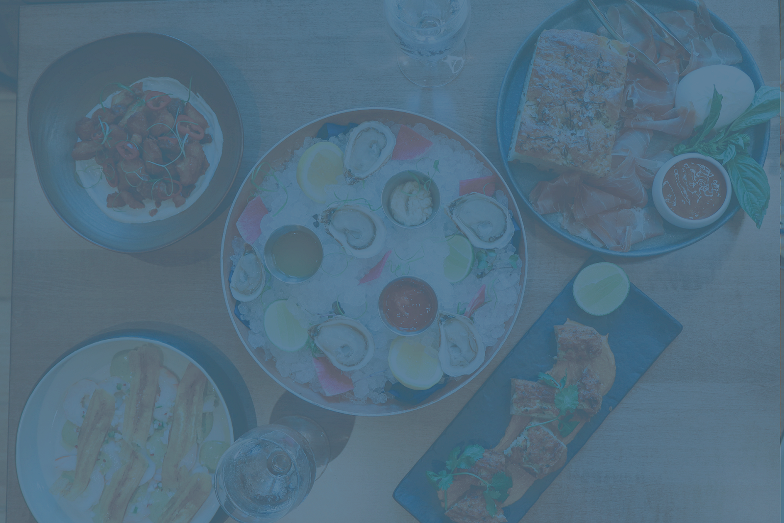 A table with various dishes including oysters, sauces, and sliced meats, garnished with lemon and herbs.