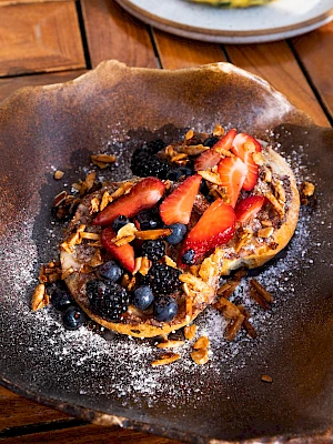 A toasted bagel topped with strawberries, blueberries, blackberries, nuts, and a dusting of powdered sugar on a rustic plate.