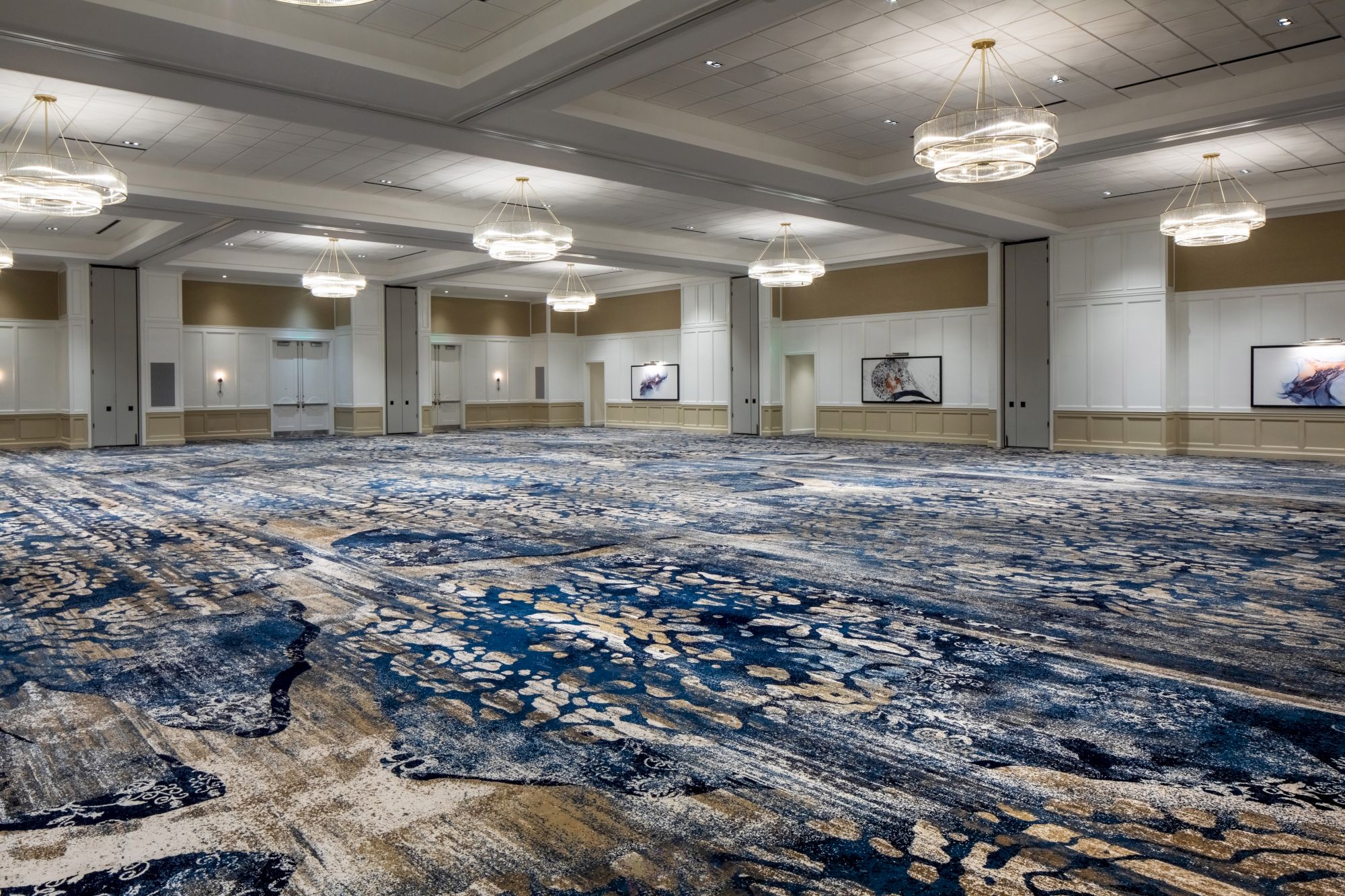 An empty, spacious conference room with abstract patterned carpet, modern chandeliers, and minimalist wall art.
