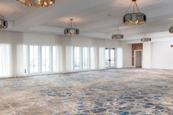 A spacious, empty room with patterned carpet, large windows, and modern chandeliers hanging from the ceiling.