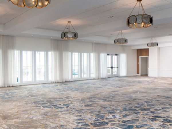 A spacious, empty room with patterned carpet, large windows, and modern chandeliers hanging from the ceiling.