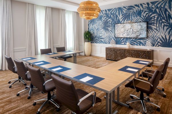 A conference room with U-shaped tables, brown chairs, blue accents, and a decorative wall, under a wicker chandelier.