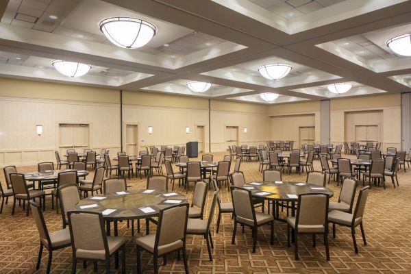 An empty conference room with round tables and chairs, well-lit with overhead lighting fixtures, and neutral-colored walls.