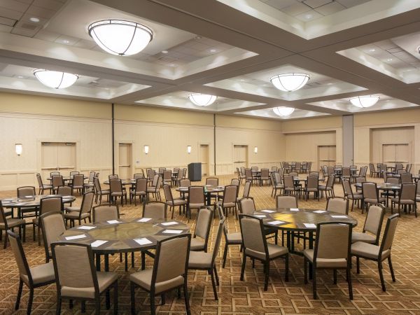 An empty conference room with round tables and chairs, well-lit with overhead lighting fixtures, and neutral-colored walls.