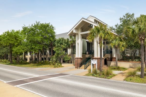 A large building with a modern design, surrounded by trees and greenery, located by a road.