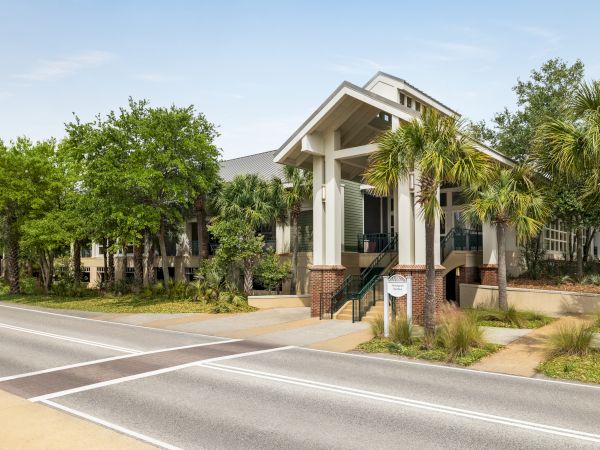 A large building with a modern design, surrounded by trees and greenery, located by a road.