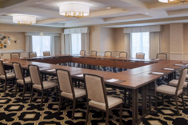 The image shows a conference room set up with a U-shaped table arrangement, surrounded by chairs, and decorated with patterned carpet.