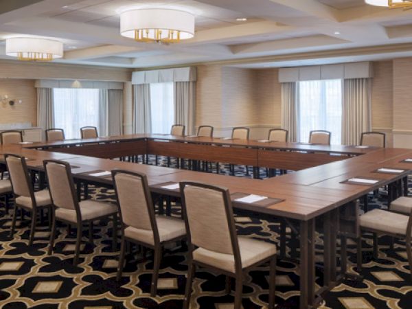 The image shows a conference room set up with a U-shaped table arrangement, surrounded by chairs, and decorated with patterned carpet.