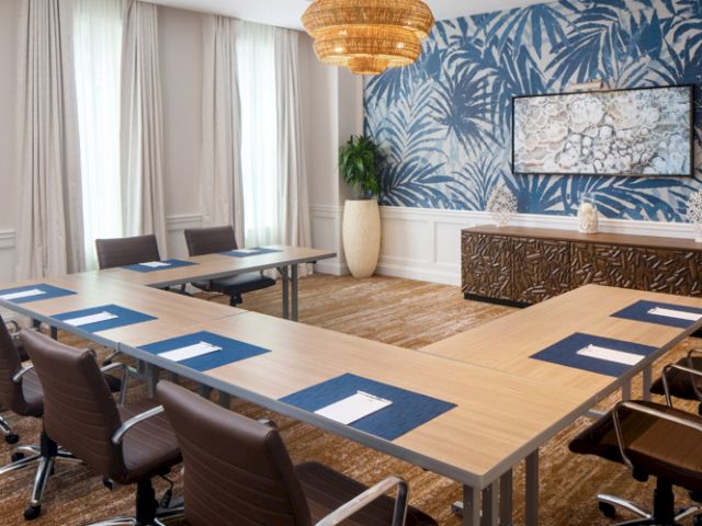 A meeting room with an elegant U-shaped table setup, cushioned chairs, wall art, blue-themed wallpaper, and modern lighting.