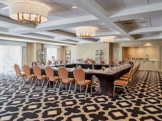 A modern conference room setup with a U-shaped table arrangement, orange chairs, and patterned carpet is shown in the image.