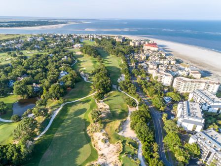 This image shows an aerial view of a coastal area with a golf course, residential buildings, and a beach beside the ocean.