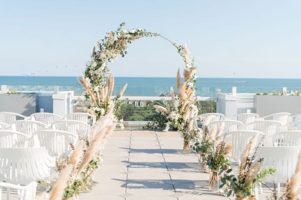 An outdoor wedding setup with a floral archway, white chairs, and ocean view.