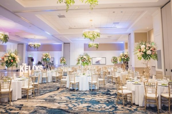 An elegantly decorated event hall with round tables, floral centerpieces, and chairs; ambient lighting creating a welcoming atmosphere.