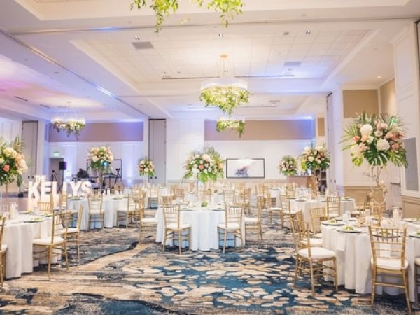 An elegantly decorated event hall with round tables, floral centerpieces, and chairs; ambient lighting creating a welcoming atmosphere.