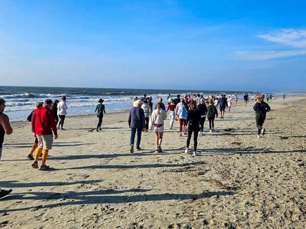 A sunny beach scene with people walking along the sandy shore toward the ocean under a clear blue sky.