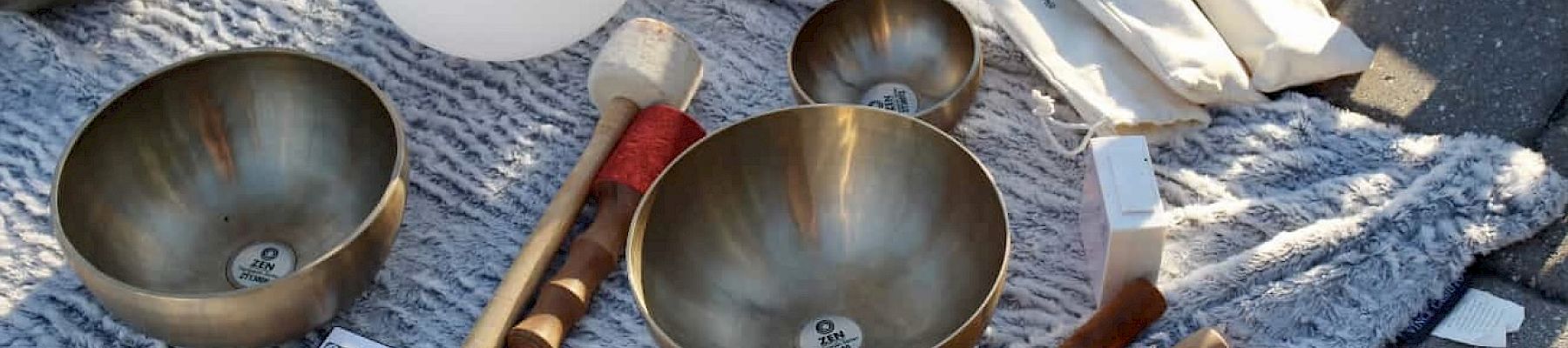 The image shows a collection of singing bowls, mallets, a notebook, and cloth laid out on a textured surface.
