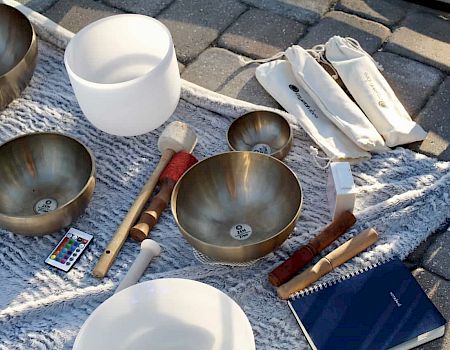 The image shows a collection of singing bowls, mallets, a notebook, and cloth laid out on a textured surface.
