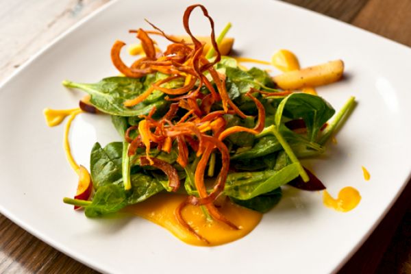 A salad with spinach leaves, thin carrot strips, and sauce, artfully arranged on a square white plate.