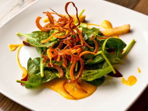 A salad with spinach leaves, thin carrot strips, and sauce, artfully arranged on a square white plate.