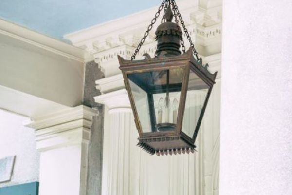 A vintage lantern hanging by chains from the ceiling near classical architectural columns.