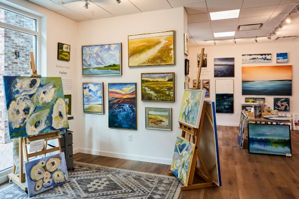 The image shows an art gallery with multiple landscape and abstract paintings on walls and easels.