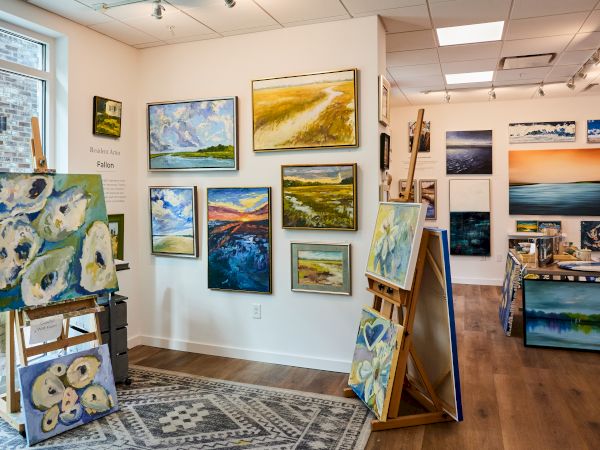The image shows an art gallery with multiple landscape and abstract paintings on walls and easels.