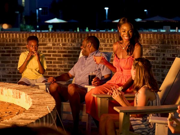 A group of people gathered around an outdoor fire pit at night, enjoying each other's company and conversation.