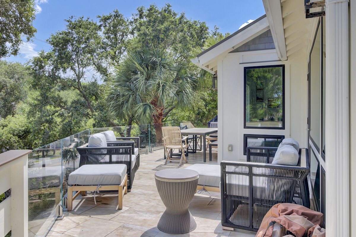 A terrace with outdoor seating, glass railing, and greenery in the background under a clear blue sky.