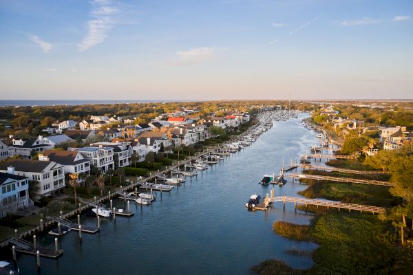 This image shows a scenic waterfront neighborhood with houses, docks, and boats lining a calm river or canal under a clear sky.