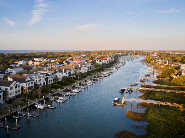 This image shows a scenic waterfront neighborhood with houses, docks, and boats lining a calm river or canal under a clear sky.