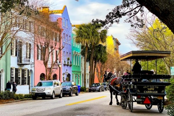 A colorful street with pastel buildings, parked cars, and a horse-drawn carriage under tree-lined surroundings.