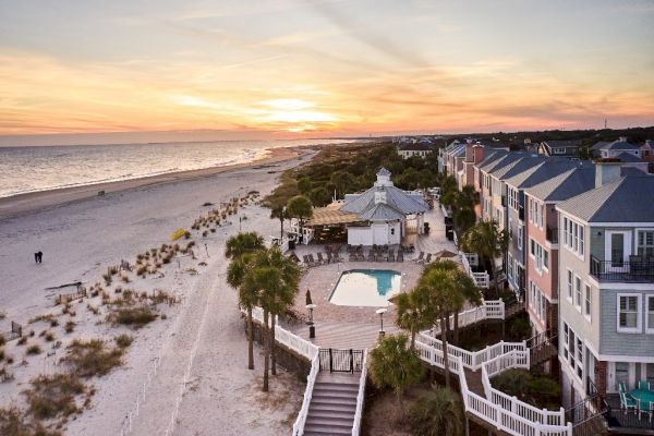 A serene beach scene at sunset, with a pool, palm trees, and colorful buildings lined along the shore.