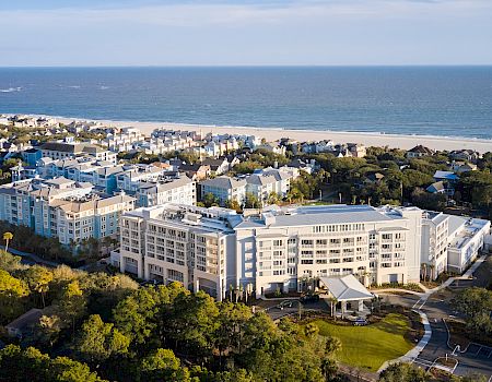 This image shows a coastal resort with several large buildings surrounded by trees and greenery, and a beach in the background.