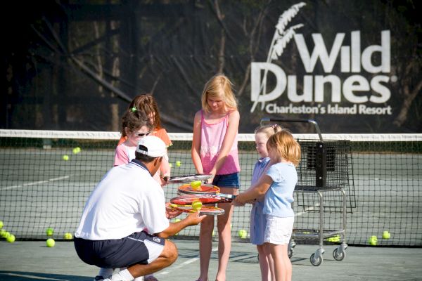 A tennis coach teaches kids on a court, with rackets and balls, at Wild Dunes Resort, Charleston.