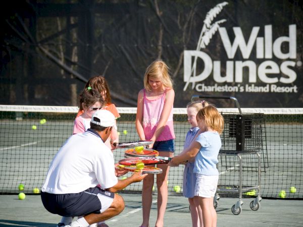 A tennis coach teaches kids on a court, with rackets and balls, at Wild Dunes Resort, Charleston.