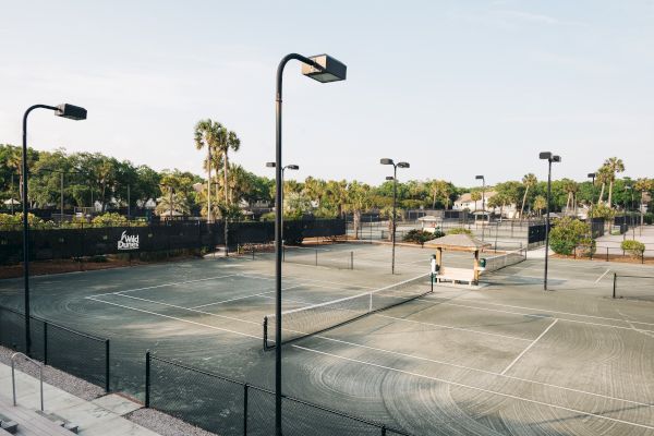 This image shows multiple outdoor tennis courts with lights, surrounded by greenery and a "Wild Dunes" sign.