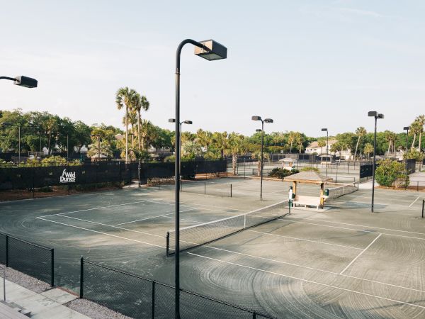 This image shows multiple outdoor tennis courts with lights, surrounded by greenery and a "Wild Dunes" sign.