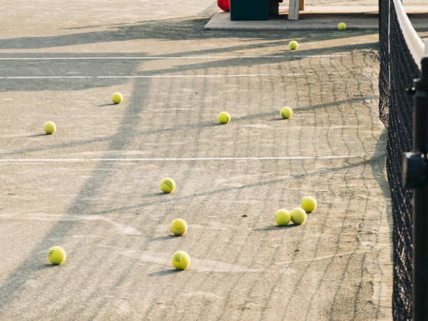 A tennis court with several tennis balls scattered around, situated next to a net under sunlight, creates a playful scene.