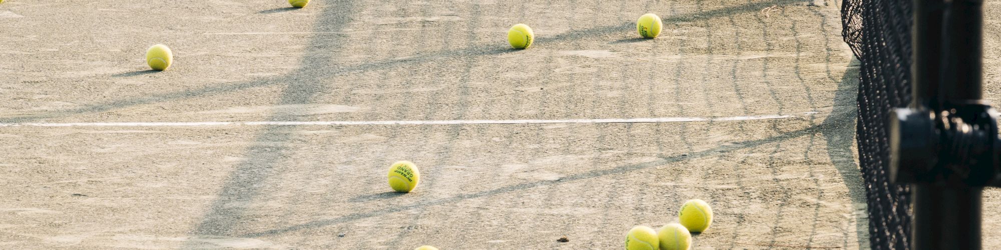 Tennis balls scattered across a tennis court with a net to the right side of the image.