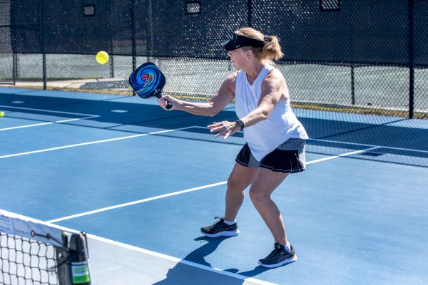 A woman is playing pickleball on a blue court, preparing to hit a ball with a paddle while wearing sports attire and a visor.