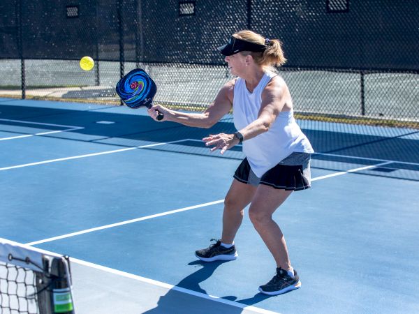 A woman is playing pickleball on a blue court, preparing to hit a ball with a paddle while wearing sports attire and a visor.