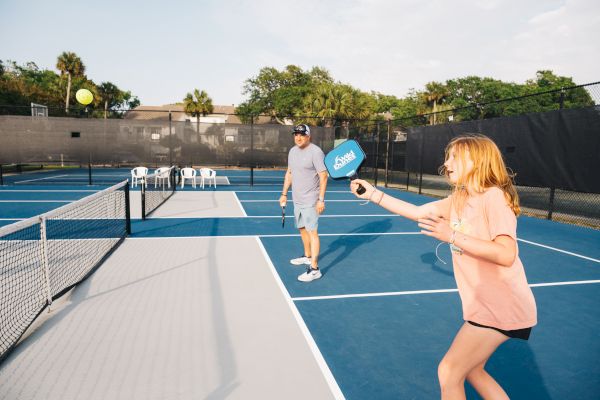 Two people playing pickleball on an outdoor court, with one about to hit the ball.