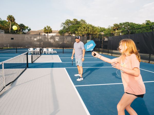 Two people playing pickleball on an outdoor court, with one about to hit the ball.