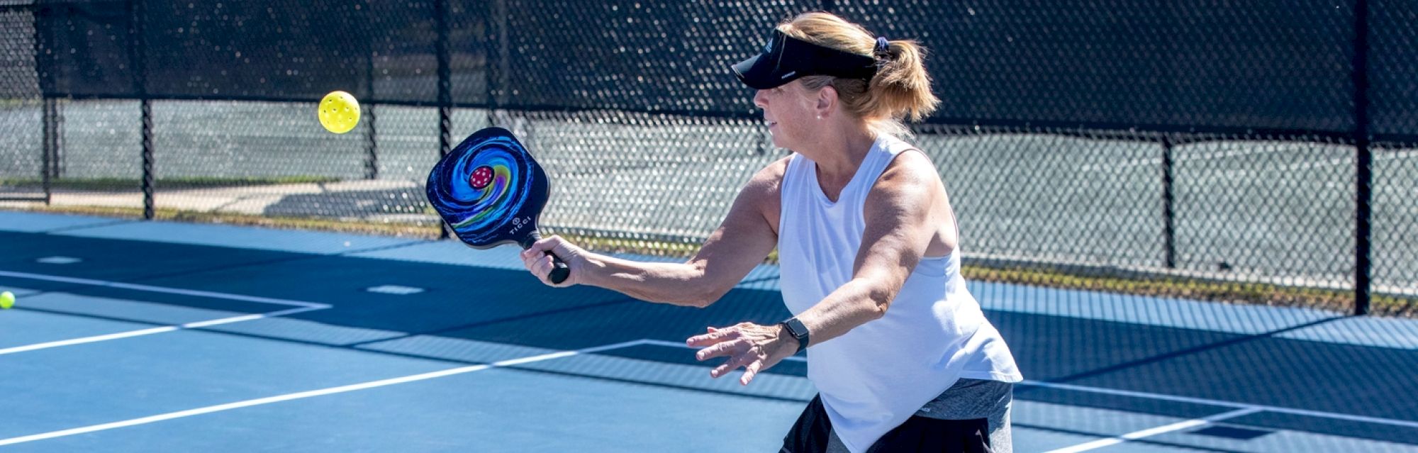 A person plays pickleball on an outdoor court, ready to hit the ball with a paddle.