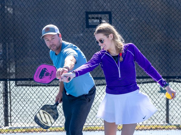 Two people are playing pickleball on an outdoor court, each holding paddles. They are focused on the game.