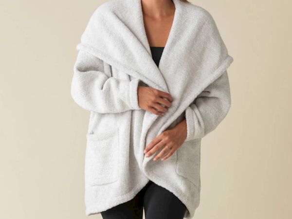 A person wears a cozy, oversized gray coat over a dark outfit, standing against a neutral background.