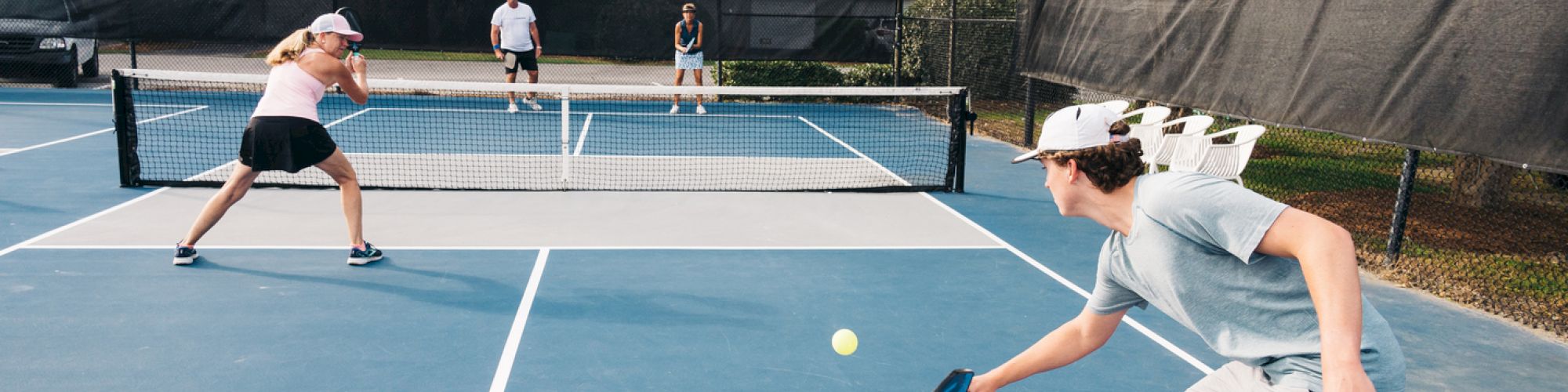 People are playing pickleball on an outdoor court, focusing on the ball, with a doubles match in progress.