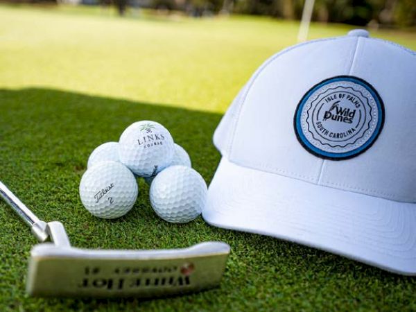 A golf-themed image featuring a white cap, several golf balls, and a putter on the green grass of a golf course.